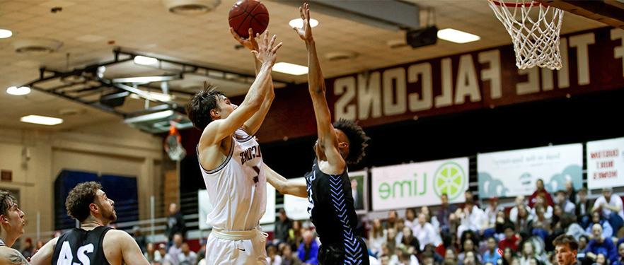 An SPU men's basketball player shoots into the hoop while an opposing player goes up for a block.